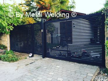 Modern black metal gate with horizontal slats in a garden setting.