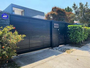 Modern house behind a black metal fence with address 6684 and security sign.