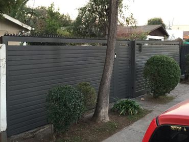 Modern gray metal fence with sharp spikes and trimmed bushes outside a residential property.