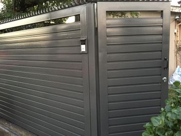 A modern gray metal gate with horizontal slats and a doorbell.