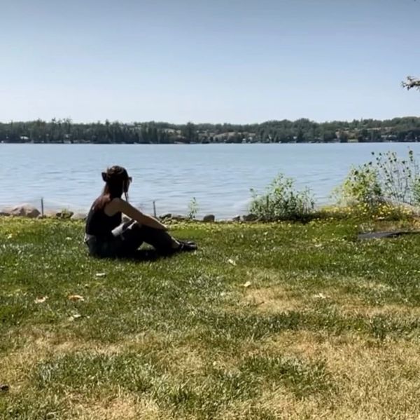 Person sitting on grass by a calm lake under clear sky.