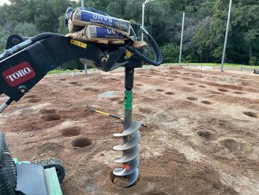 A Toro auger drilling holes in the ground at a construction site.