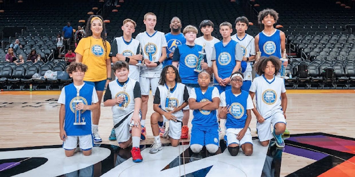 Youth basketball team posing with trophies on court after game.