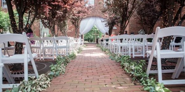 Outdoor wedding aisle with white chairs and greenery.