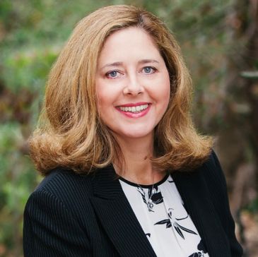 Smiling woman with blonde hair in professional attire outdoors.