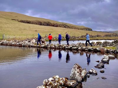 A group of people with dogs on leads, crosses a causeway over a Scottish loch