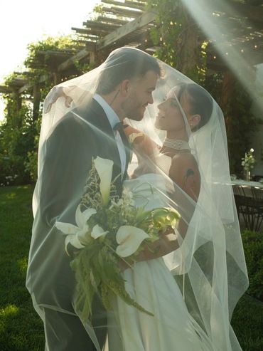 Bride and groom sharing a romantic moment under the veil during their outdoor wedding.