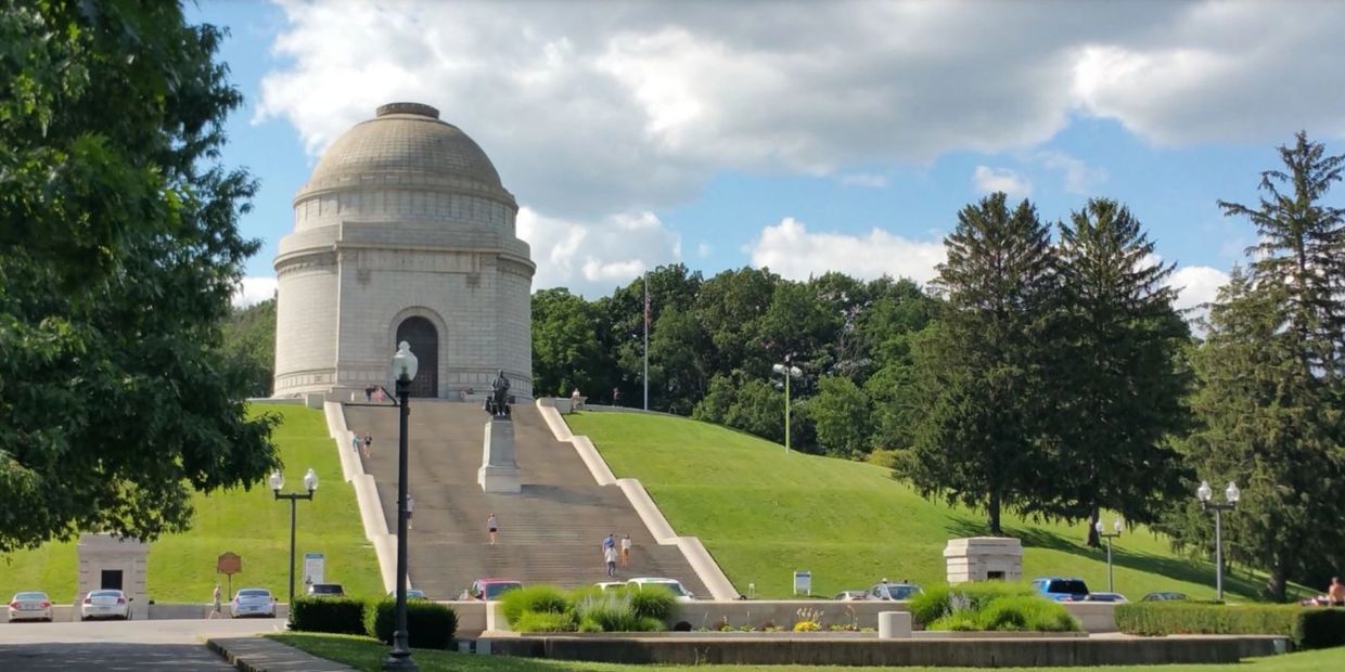 A large dome-shaped monument on a grassy hill with stairs.