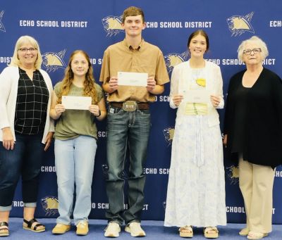 Three students holding certificates with two women in a school district setting.