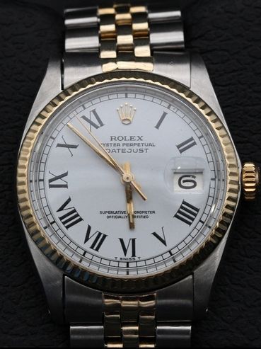 Close-up of a Rolex Datejust watch with gold and silver band on a black textured surface.