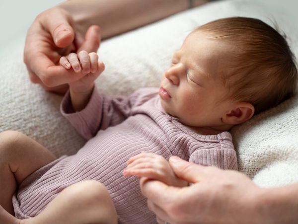 Newborn baby peacefully sleeping while holding an adult's fingers.