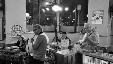 A four-member band performs live in a cozy bar setting with colorful lighting.