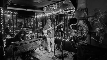 A jazz band performs in a cozy, warmly lit venue decorated with string lights and mirrors.