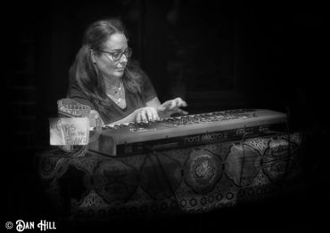 Woman playing a Nord Electro 2 keyboard with a tip jar beside her.