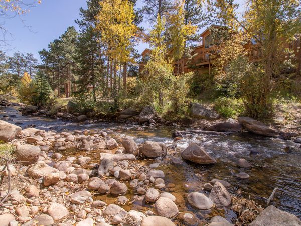 A rocky creek flowing beside autumn trees and wooden houses.