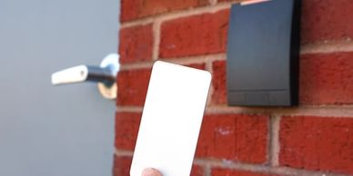 Hand holding a white key card near a door access panel on a brick wall.