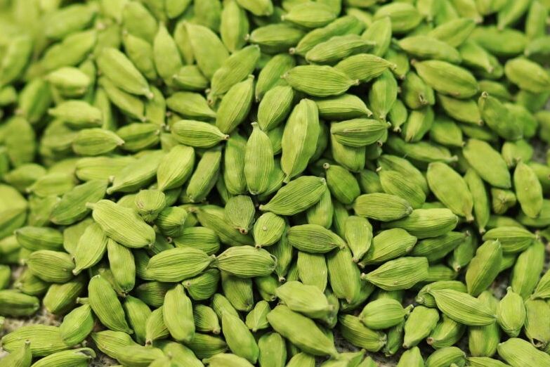 Close-up of fresh green cardamom pods piled together.