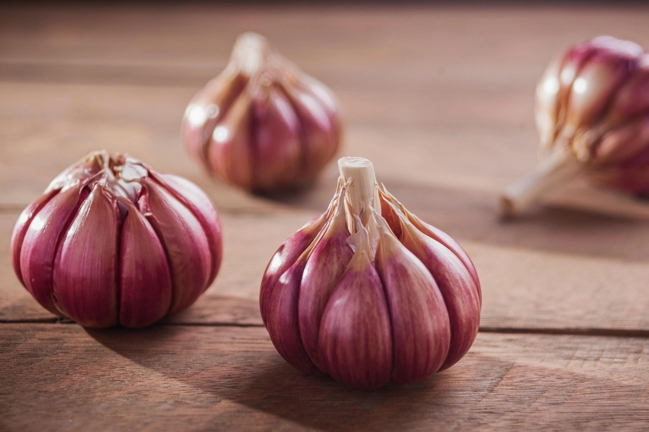 Close-up of purple garlic bulbs on wooden surface.