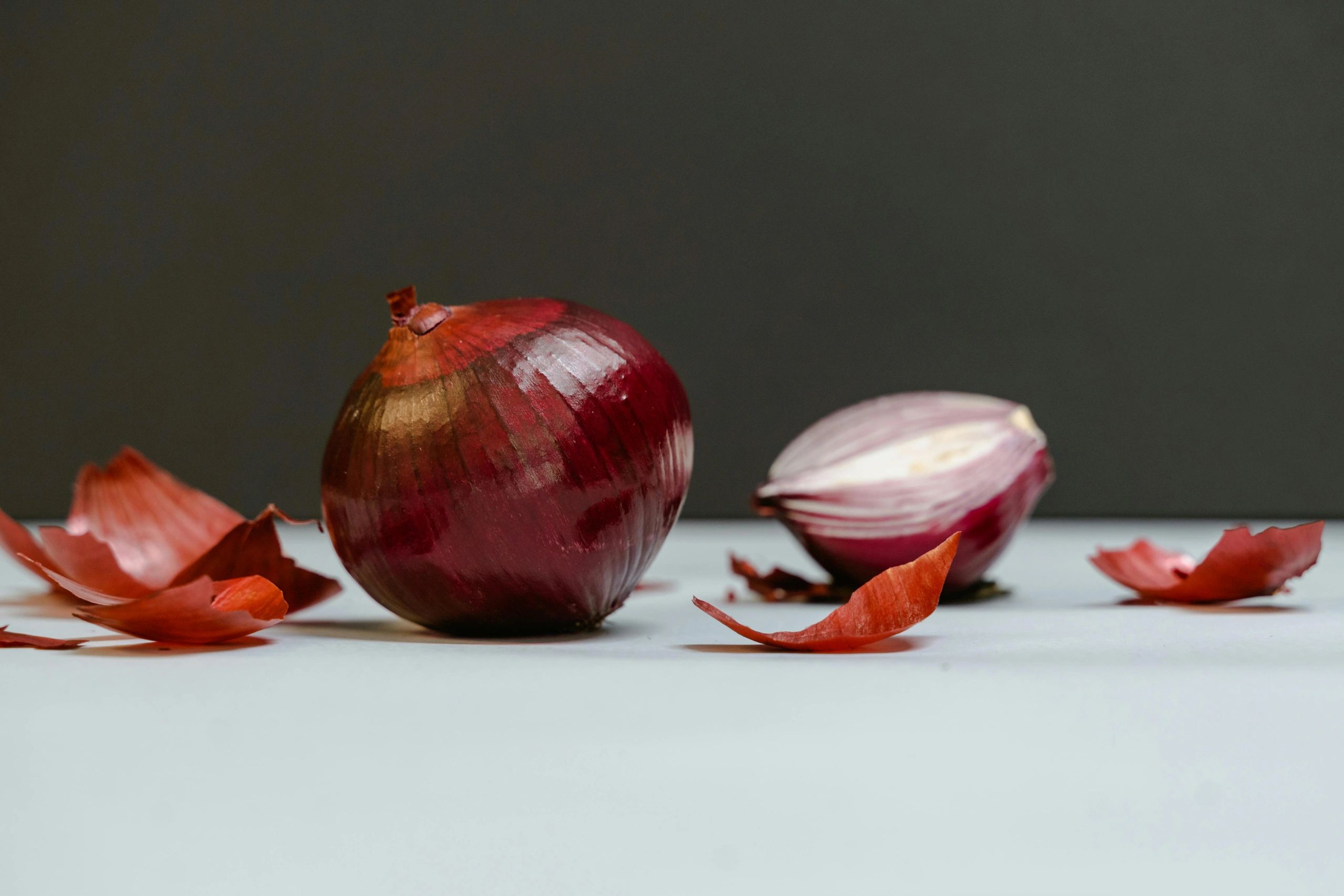 Whole and halved red onions with scattered onion skins on a white surface.