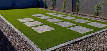 Artificial turf installation with square paver stepping pads and a clean paver border.