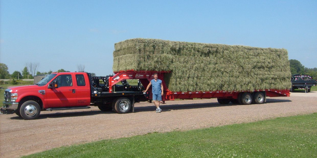 Owner, Pete, stands next to his truck and gooseneck trailer loaded full of hay.