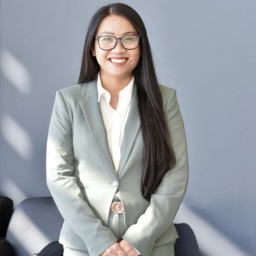 Smiling woman in a grey suit and glasses sitting confidently.