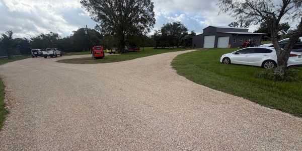 A spacious gravel driveway with vehicles and trees.