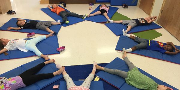 Children reclined on yoga mats in a circular shape.