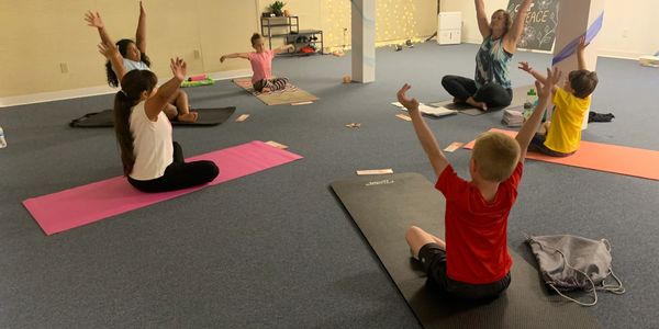 Children on yoga mats sitting upright and reaching arms overhead.