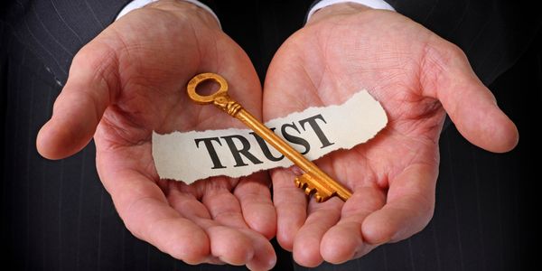 Hands holding a gold key and a paper with the word TRUST.