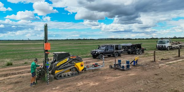 Man operating machinery in a vast rural field with trucks and equipment nearby.