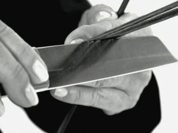 Person sharpening a knife with a sharpening rod in black and white.