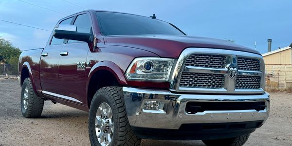 Maroon RAM pickup truck parked on a dirt road with a clear sky.