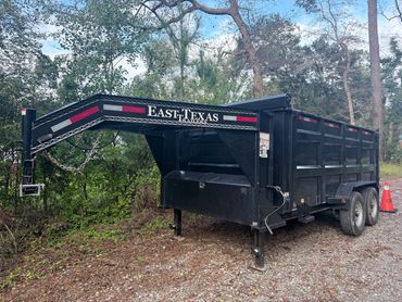 Black East Texas trailer parked on gravel with trees in background.