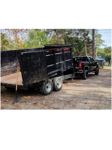 Black pickup truck towing a large black dump trailer with a shovel leaning against it.