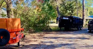 Three trailers parked on a gravel road surrounded by trees.