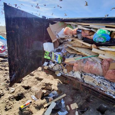 Dump trailer unloading construction debris under a blue sky with flying seagulls.