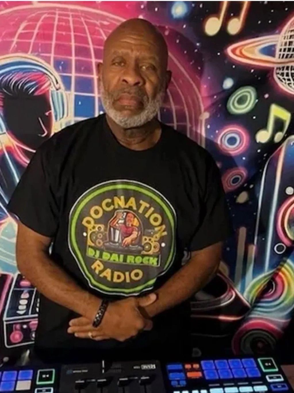 Man in DJ gear with colorful music-themed mural background.