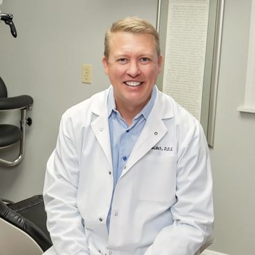 Smiling male dentist in white coat in clinic.