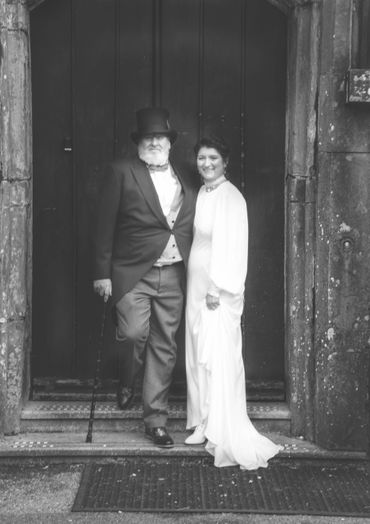 A couple dressed in vintage formal attire poses on stone steps.