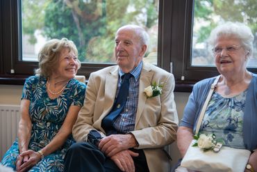 Three elderly people sitting and smiling indoors by a window.