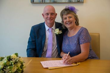 A happy couple signing a document, dressed elegantly for a special occasion.