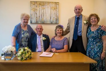 Five people posing for a formal photo with a bouquet and document on the table.