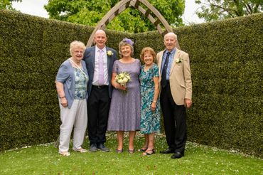 Group of five people posing under a wooden arch in a garden.
