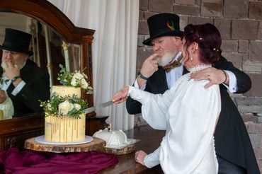 Couple in vintage attire cutting a decorated wedding cake together.