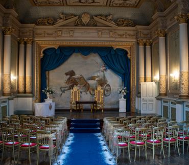Ornate wedding venue with gold chairs and blue aisle.