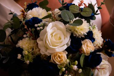 Elegant bouquet with white, cream, and deep blue flowers accented by green leaves.