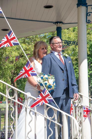 Bride and groom standing on a decorated gazebo with Union Jack flags.