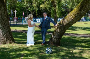 Bride and groom hold hands in a sunny park with wedding bouquet on the grass.