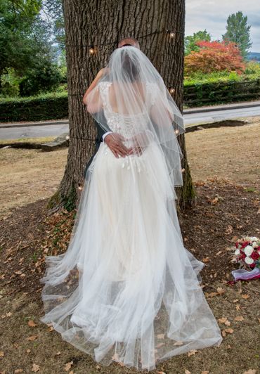 Bride and groom embracing near a tree adorned with fairy lights outdoors.